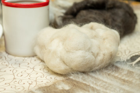 Soft wool fibers and red-rimmed mug on ornate tablecloth.