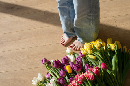 Barefoot woman standing beside a colorful array of tulips on a wooden floor. Casual lifestyle flat lay with copy space for designの写真素材