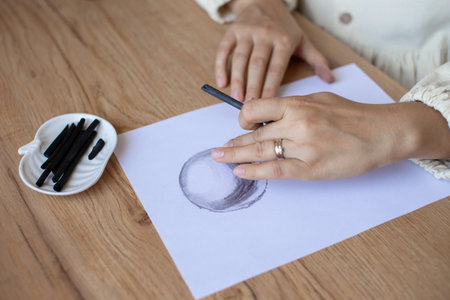 Close-up shot of a woman's hand drawing a perfect circle on a blank sheet of paper with a black marker, with extra markers on the sideの写真素材