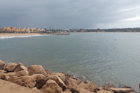 Overcast clouds loom above a tranquil sea beside a sandy beach, capturing the calm before a coastal...