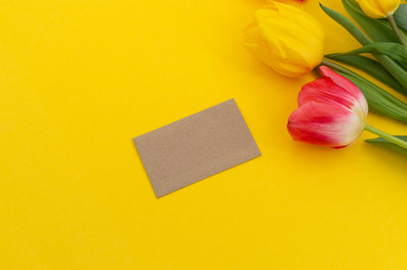 A vibrant setting featuring colorful tulips beside a blank card, ready for a personalized message, against a yellow backdropの写真素材