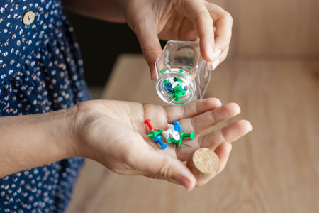 An up-close shot of a person's hands carefully clasping a transparent glass jar filled with colorful paper clipsの写真素材