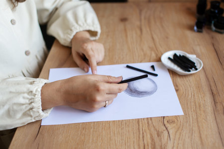 Close-up view of hands skillfully drawing with charcoal on a blank paper, next to art supplies on a wooden surfaceの写真素材