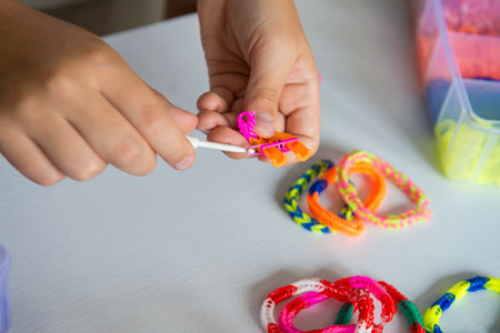 Child crafting colorful loom bands with hook on white table.の写真素材