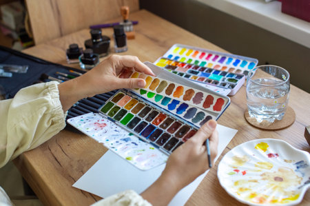 Close-up image of an artist's hands selecting colors from a vibrant watercolor palette for a new artworkの写真素材
