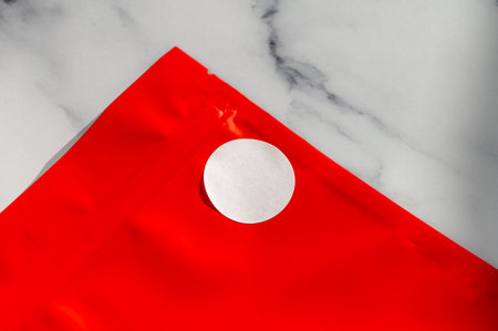 Red packaging pouch with white circular sticker on a marble surface. Top view product packaging mockupの写真素材