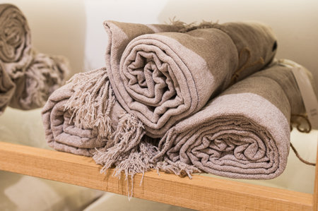 Three rolled-up beige throws with fringes displayed on a wooden shelf.の写真素材