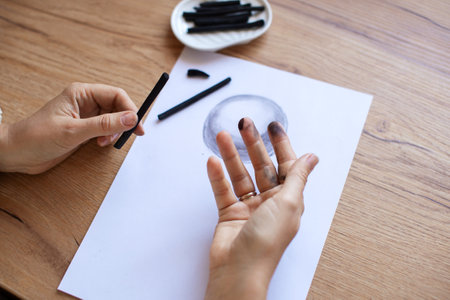 Close-up image of an artist's hand covered in charcoal as they draw a monochromatic artwork, showcasing the creative processの写真素材