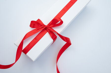 Elegant white gift box with red ribbon on white surface.の写真素材