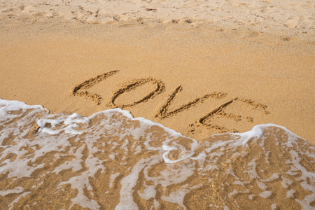 Love written in sand near ocean waves on a sandy beach.の写真素材