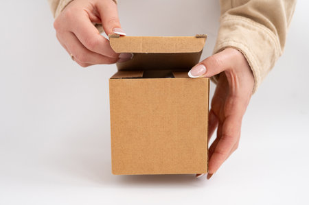 Female hands opening small brown cardboard box on white background.の写真素材