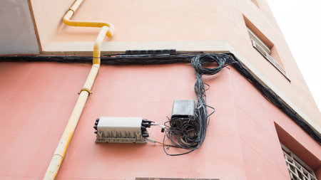 Exposed electrical cables and equipment on colorful urban building wall.