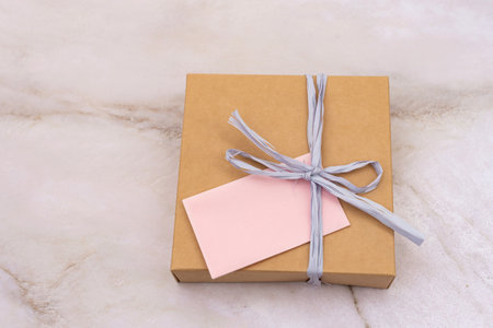 An elegantly wrapped gift box with a pink note tied by a string, presented against a soft marble...