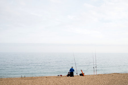Solitary fishing on tranquil beach under overcast sky.
