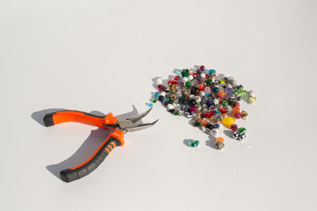 Orange handheld pliers and colorful beads on white background.の写真素材