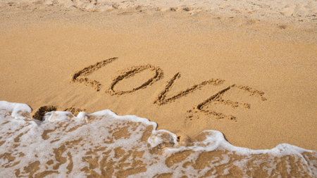 Love written on sandy beach with ocean waves approaching.の写真素材