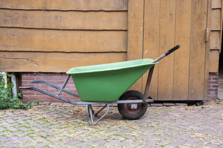 Green wheelbarrow against wooden wall in rustic outdoor setting.