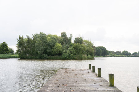 Serene lake view with wooden pier and lush green island in tranquil landscape.の写真素材