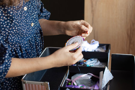 A woman meticulously organizes her sewing items, including threads and fabrics, in a home craft area, showcasing creativity and organizationの写真素材