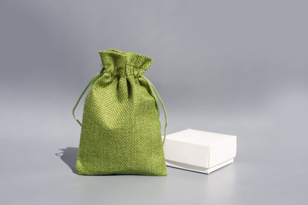 Green fabric drawstring bag and white box on gray background.の写真素材