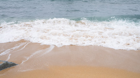 Gentle waves lapping onto sandy beach shoreline with clear blue ocean waters.