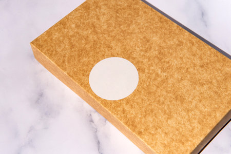 Brown cardboard box with white circle label on marble surface.の写真素材