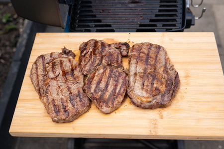 Grilled steaks resting on wooden board by outdoor grill.の写真素材