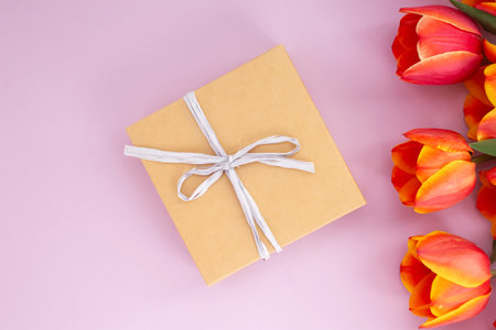 Gift box with bow and tulips on pink background.