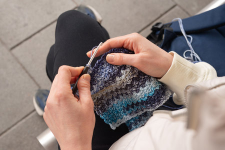 Adult female crocheting with blue yarn outdoors in casual attire.