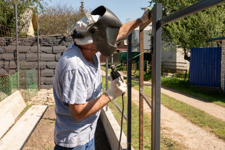 Elderly caucasian male welding outdoor metal fence construction.