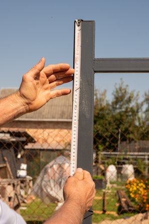 Adult male measuring metal fence with tape measure in garden setting.の写真素材