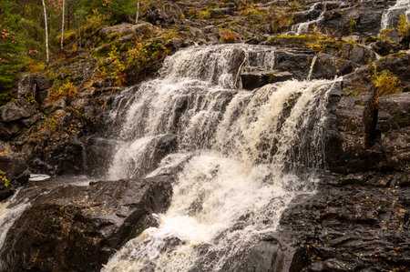 Cascading waterfall over rocky terrain in autumn forest scenery.の写真素材