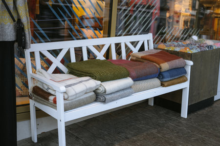 Cozy assorted blankets on white bench outside shop.の写真素材