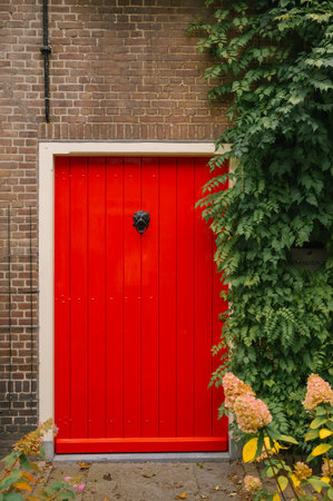 Bright red door on brick wall with lush green ivy and yellow flowers.の写真素材