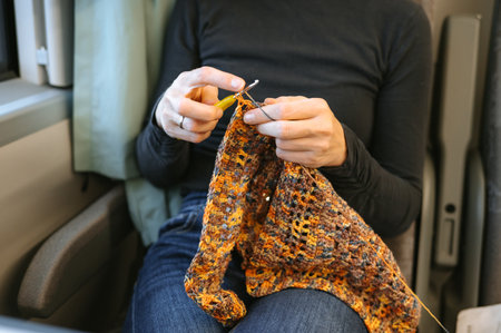 Female adult crocheting colorful scarf on train journey.