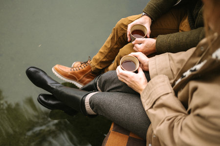 Couple enjoying coffee by the water in autumn attire.の写真素材