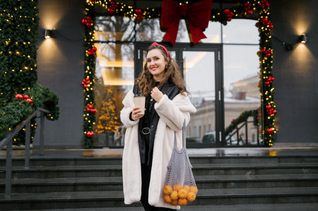 Young caucasian female holding oranges and coffee in festive urban setting.の写真素材