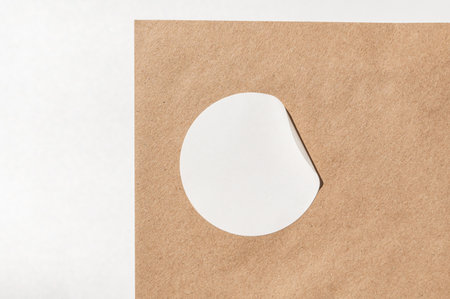 White circle sticker partially peeled on brown paper surface.の写真素材