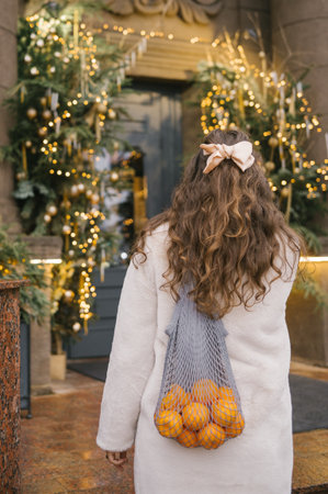 Young caucasian female carrying oranges in mesh bag during festive holiday season.の写真素材