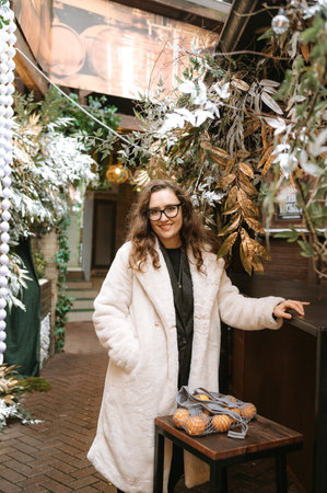 Caucasian young female in winter coat at festive outdoor market with oranges.の写真素材