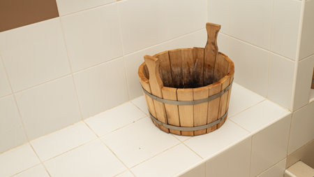 Wooden bucket with handles on white tiled bathroom surface.の写真素材