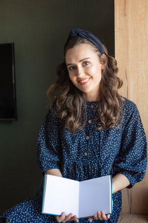 Capture your audience with this image of a woman in a patterned shirt holding an open book with a blank page, ideal for custom messagesの写真素材
