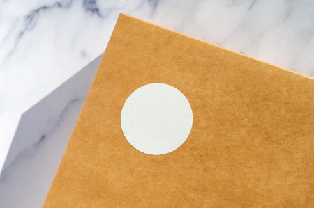 Close-up image of a simple brown paper package with a round white sticker label, evoking minimalist and eco-friendly packaging conceptsの写真素材