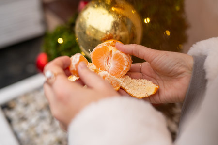 Close-up of female hands peeling orange with Christmas decorations in background.の写真素材