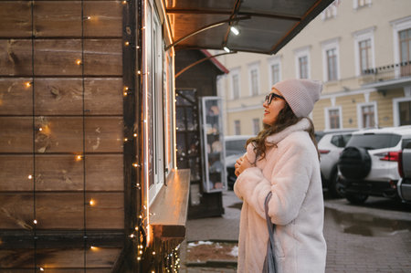 Young caucasian woman in warm winter clothes ordering at a festive street food stall.の写真素材