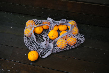 Fresh oranges in gray mesh bag on wooden floor.の写真素材