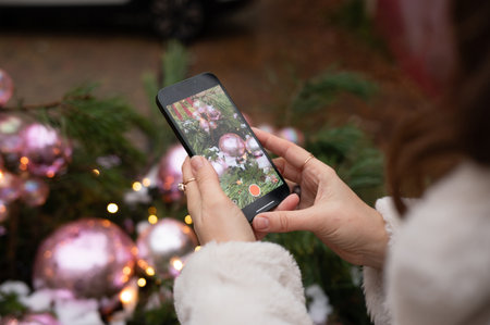Woman capturing christmas decorations on smartphone outdoors.の写真素材