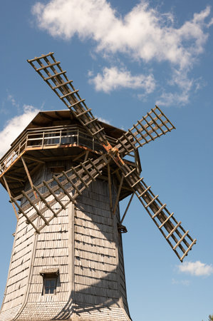 Historic wooden windmill against blue sky with clouds.の写真素材