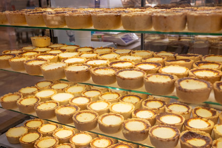 Rows of delicious custard tarts on glass shelves in bakery display.の写真素材