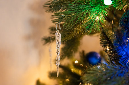 Icicle ornament hanging on decorated christmas tree branch.の写真素材